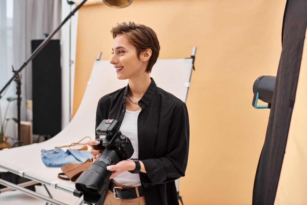 cheerful beautiful female photographer in everyday clothing working with her equipment at studio